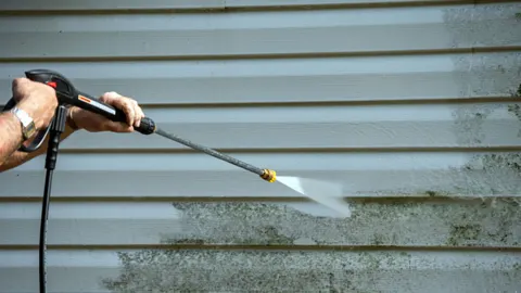 Pressure washer removing algae from vinyl siding